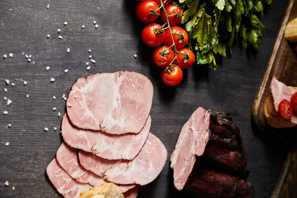 top view of tasty ham sliced ham, cherry tomatoes, parsley, salt on wooden grey table