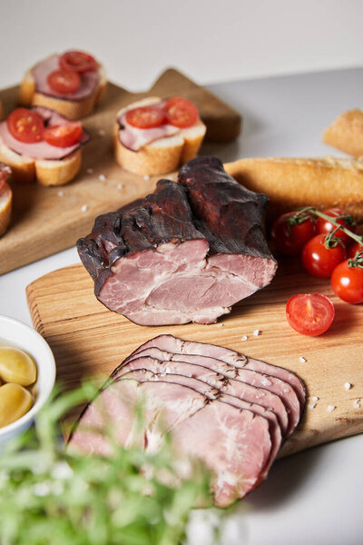 selective focus of tasty ham on cutting board with cherry tomatoes, olives and baguette near canape