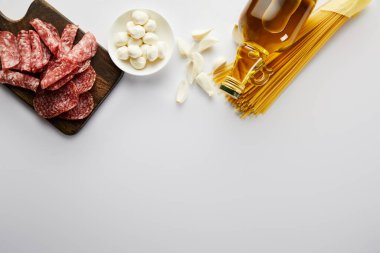 Bir şişe zeytinyağı, et tabağı, sarımsak, makarna ve beyaz mozzarellalı kase.  