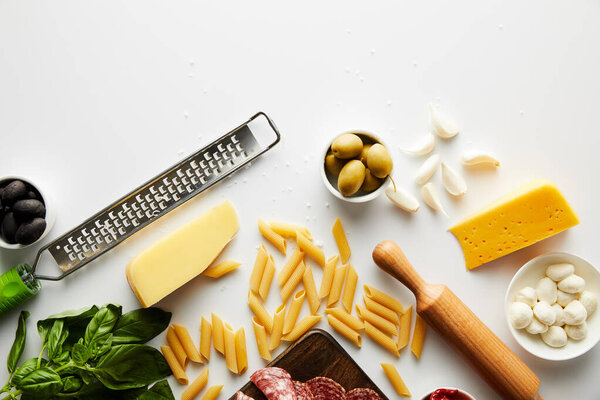 Top view of grater, rolling pin, pasta and ingredients on white background 