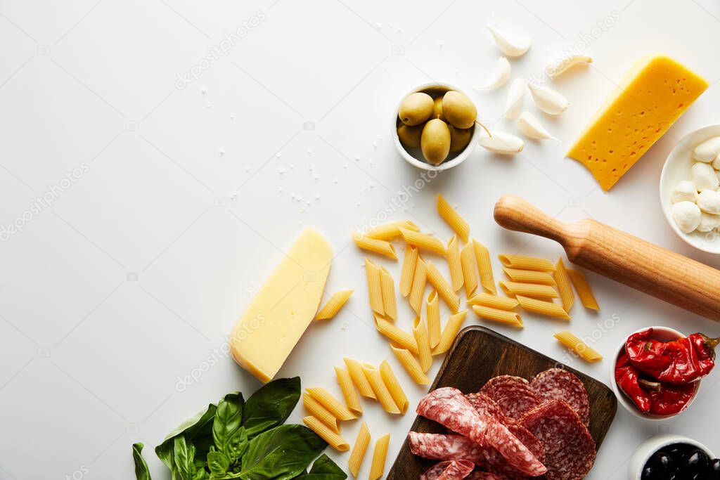 Top view of meat platter, rolling pin, pasta and ingredients on white background 