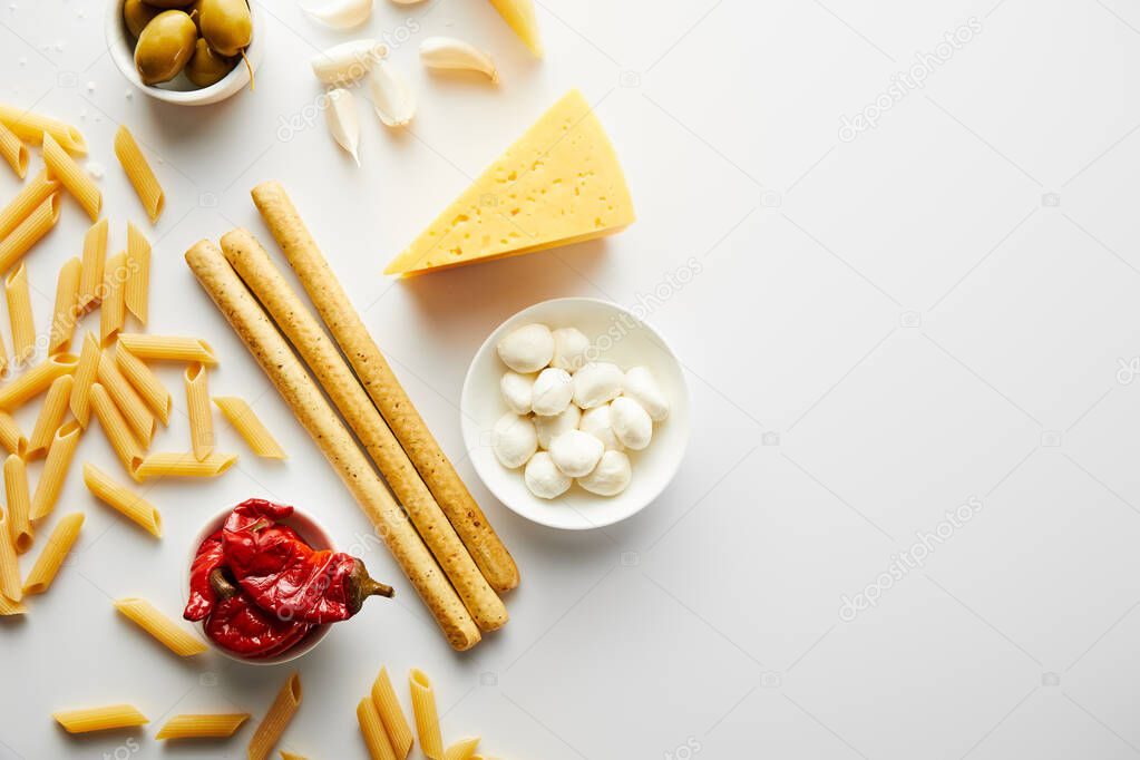 Top view of breadsticks, pasta and ingredients on white background 