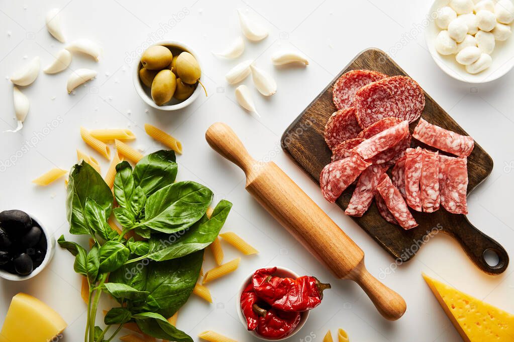 Top view of meat platter, rolling pin, basil leaves and ingredients on white background 