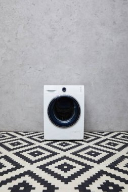 Gri duvarın yanında modern çamaşır makinesi ve banyoda süs halısı. 