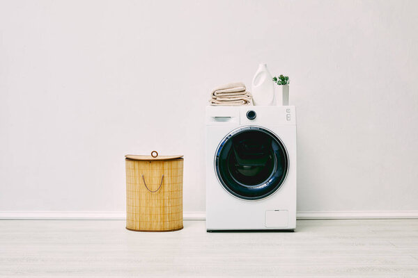 detergent bottle, towels and plant on modern washing machine near laundry basket in bathroom 