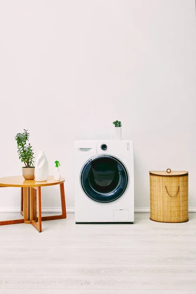 バスルームのコーヒーテーブル 洗濯バスケット 現代の洗濯機の近くの緑の植物やボトル — ストック写真