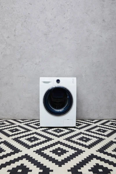 modern washing machine near grey wall and ornamental carpet in bathroom