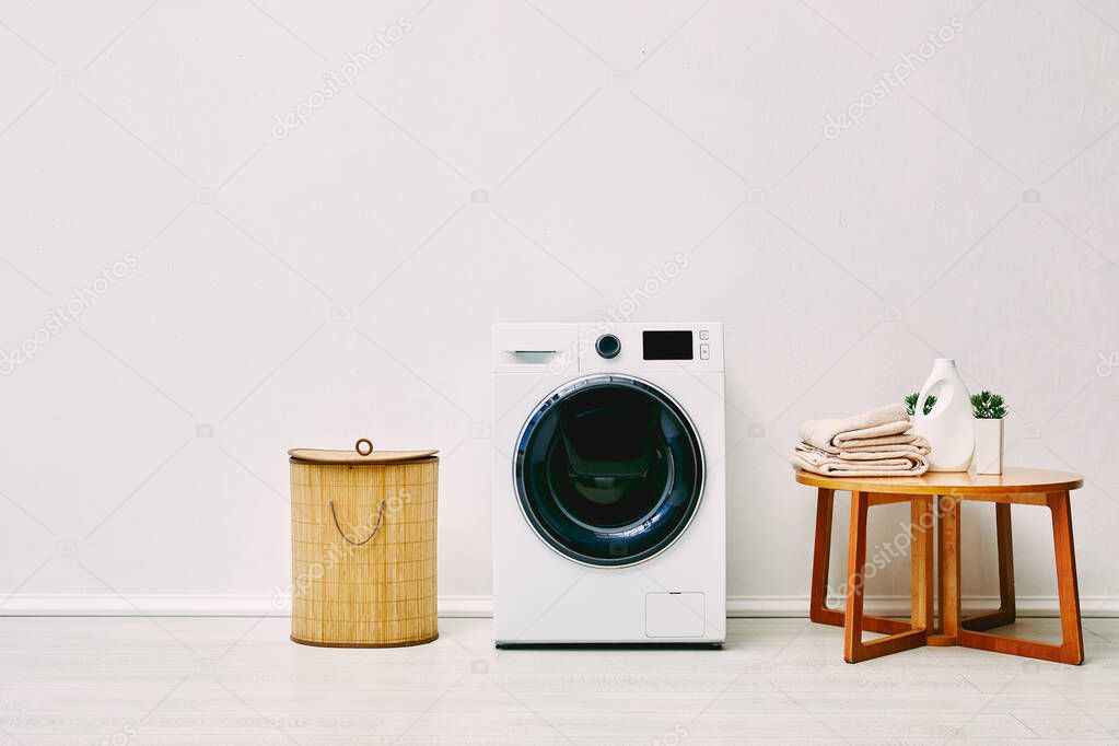 white washing machine near laundry basket, coffee table with towels, detergent bottle and plant in bathroom 