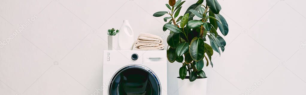 panoramic shot of modern bathroom with plants near detergent bottle and towels on washing machine