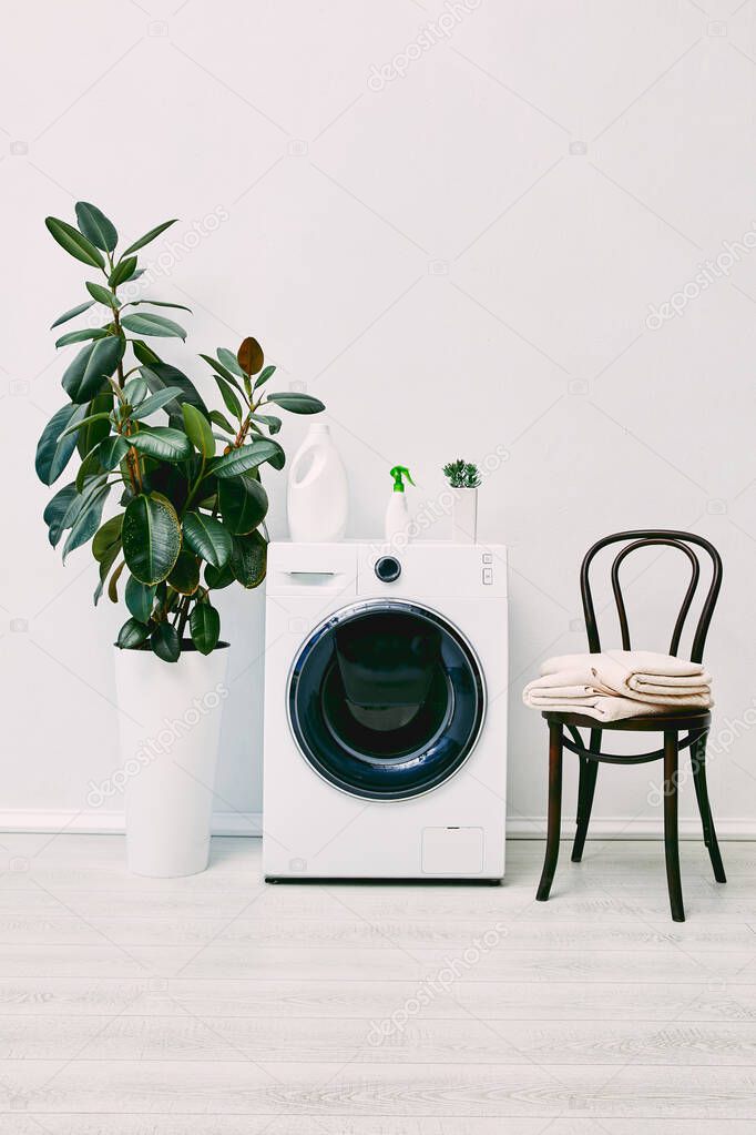 modern bathroom with plants, detergent and spray bottles, towels and chair near washing machine