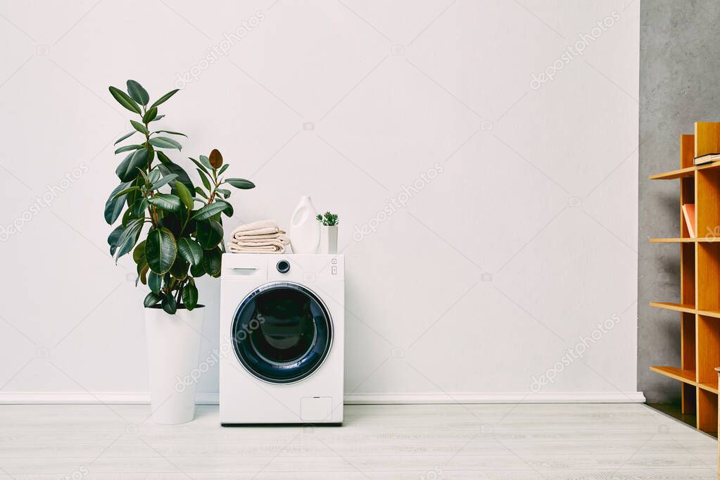 modern bathroom with plants, detergent bottle, towels and chair near washing machine and wooden rack
