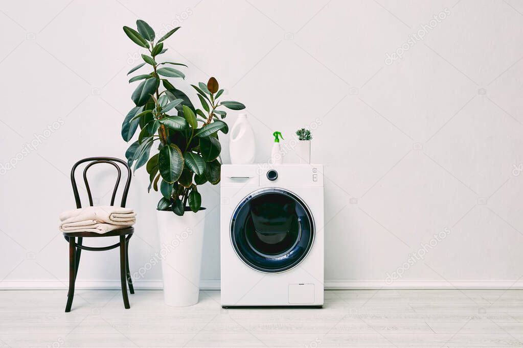 green plants near washing machine with bottles near chair with towels 