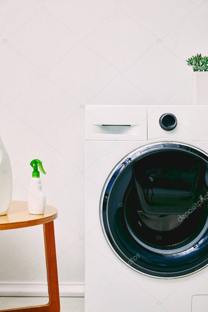 detergent bottles on coffee table near modern washing machine and plant in bathroom 