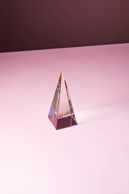 Pembe zemin üzerinde ışık yansıması olan şeffaf kristal piramit