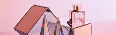 Parfüm şişesinin yanında kristal şeffaf piramit ve pembe arka planda ayna küpleri, panoramik mahsul