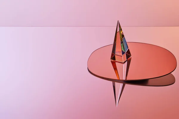 在粉色背景上的圆形反射镜上的晶体透明金字塔 — 图库照片