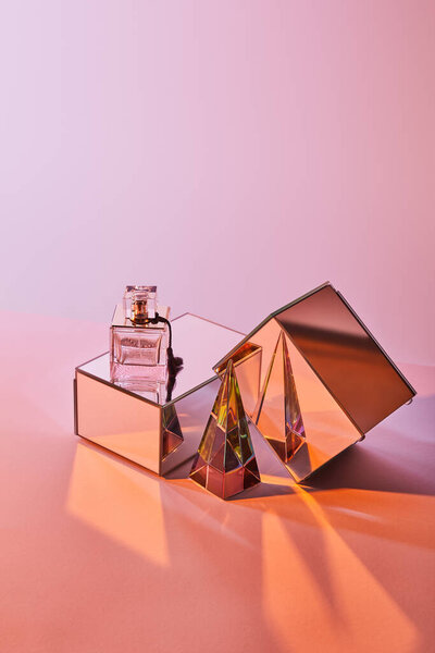 crystal transparent pyramid near perfume bottle and mirror cubes on pink background