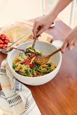 Makarna salatasıyla spatulayı karıştıran kadın manzaralı mutfak masasındaki peçetenin yanında.