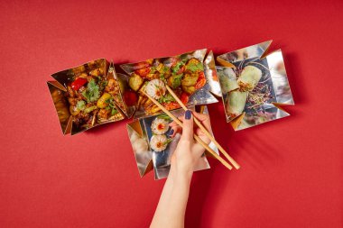 top view of woman holding chopsticks with steamed bun near prepared chinese food in takeaway boxes on red clipart