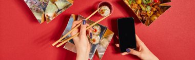 panoramic shot of woman holding chopsticks with steamed bun and smartphone with blank screen near tasty chinese food in takeaway boxes on red clipart