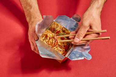 top view of man holding chopsticks near spicy noodles on red clipart