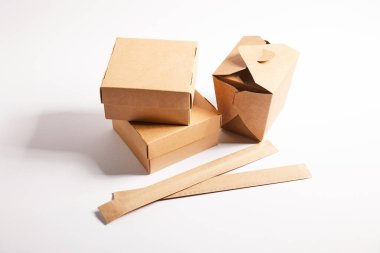 chopsticks in paper packaging near takeaway boxes with chinese food on white  clipart