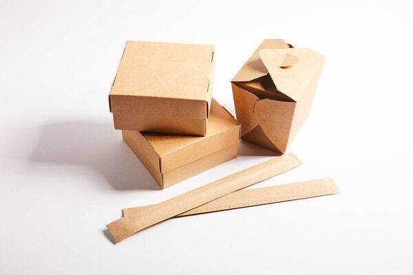 chopsticks in paper packaging near takeaway boxes with chinese food on white 