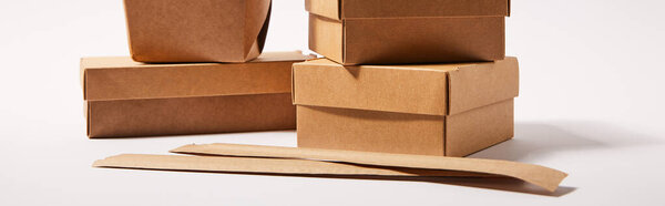 horizontal image of chopsticks in paper packaging near takeaway boxes with chinese food on white 