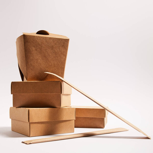chopsticks in paper packaging near takeaway boxes with prepared chinese food on white 