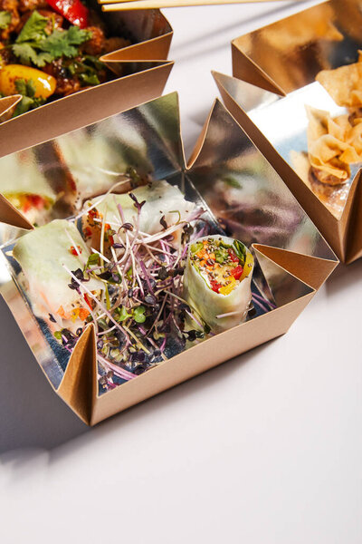 takeaway boxes with spring rolls and chinese food on white 