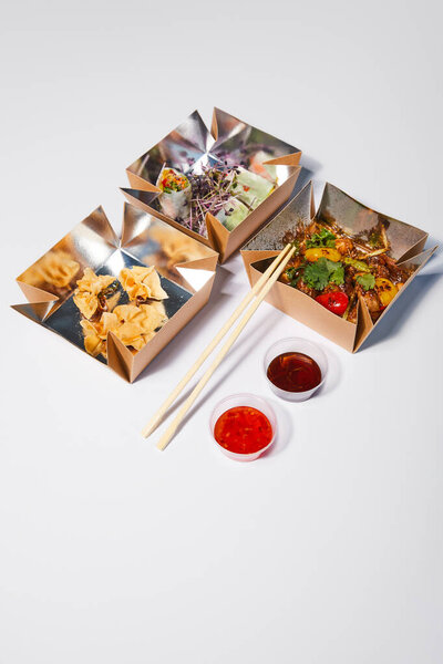 takeaway boxes with tasty and prepared chinese food near chopsticks and sauces on white 