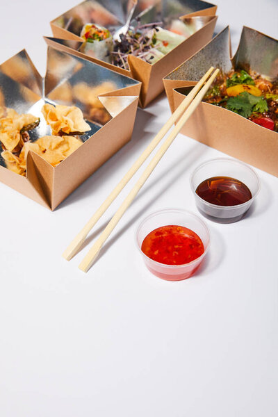 selective focus of sauces and chopsticks near takeaway boxes with prepared chinese food on white 