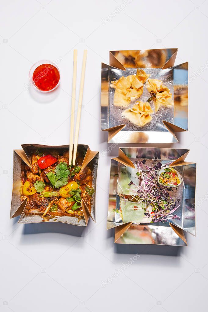 top view of takeaway boxes with chinese food near chopsticks and sauce on white 
