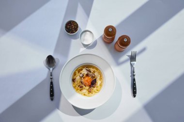Güneş ışığında beyaz masa üzerinde çatal bıçak, tuz ve biber değirmenleriyle servis edilen lezzetli carbonara makarna manzarası
