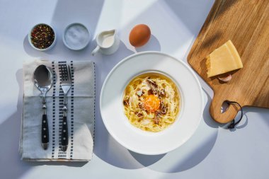 Nefis makarna soslu, çatal bıçak, baharat ve malzemelerle servis edilen beyaz masa güneşli.