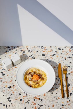 Altın çatal bıçak, tuz ve biberlikle servis edilen lezzetli carbonara makarnası.