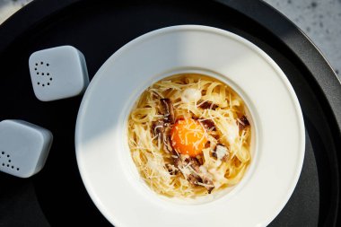 Lezzetli Carbonara Makarnası 'nın en üst görüntüsü. Siyah masada, mermer arka planda, güneş ışığında servis ediliyor.
