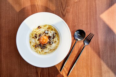 Tahta arka planda siyah çatal bıçakla servis edilen lezzetli carbonara makarna manzarası.