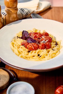 Güneş ışığında ahşap masada servis edilen domatesli, parmesanlı ve kırmızı fesleğenli lezzetli makarna.