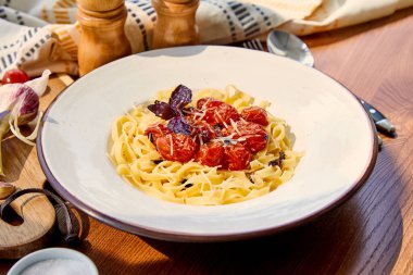 Güneş ışığında ahşap masada servis edilen domatesli, parmesanlı ve kırmızı fesleğenli lezzetli makarna.