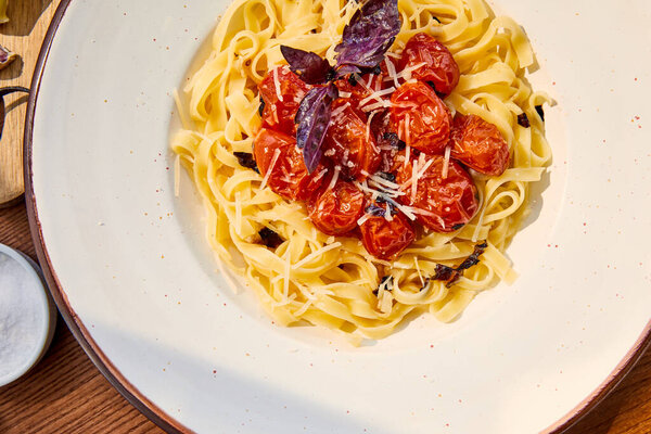 top view of delicious pasta with tomatoes served on wooden table in sunlight