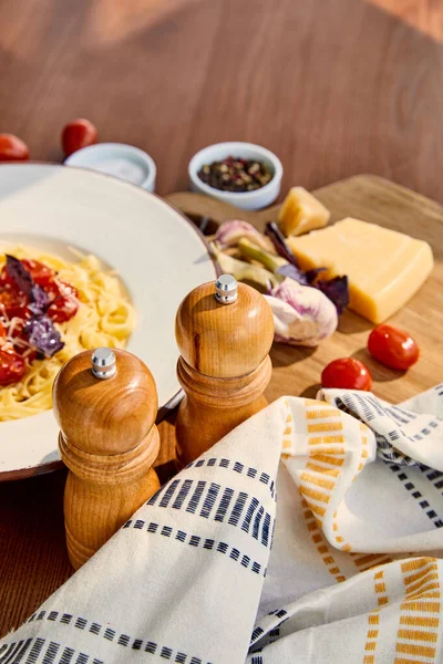 木のテーブルの上で提供されるトマトとおいしいパスタの選択的な焦点は カトラリー ナプキン 調味料や日光の下で成分 — ストック写真