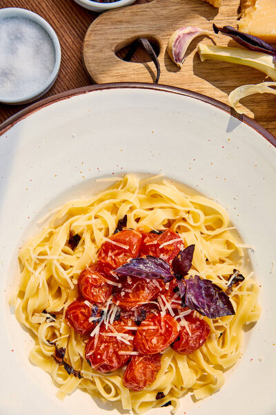 top view of delicious pasta with tomatoes served on wooden table in sunlight