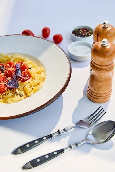 美味的意大利面 西红柿配餐具 盐和胡椒磨碎在阳光下的白桌上 — 图库照片