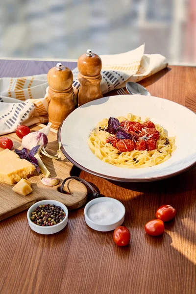 delicious pasta with tomatoes served on wooden table with napkin, seasoning and ingredients in sunlight