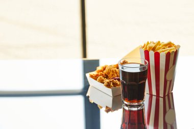 deep fried chicken, french fries and soda in glass on glass table in sunlight near window clipart