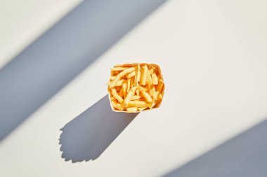 Lezzetli patates kızartmalarının üst görüntüsü kovada beyaz masada güneş ışığında