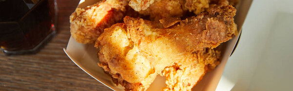 top view of deep fried chicken and soda in glass on wooden table in sunlight, panoramic orientation