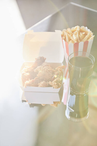 deep fried chicken, french fries and soda in glass on glass table in sunlight