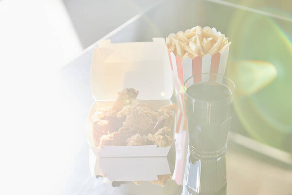 deep fried chicken, french fries and soda in glass on glass table in sunlight